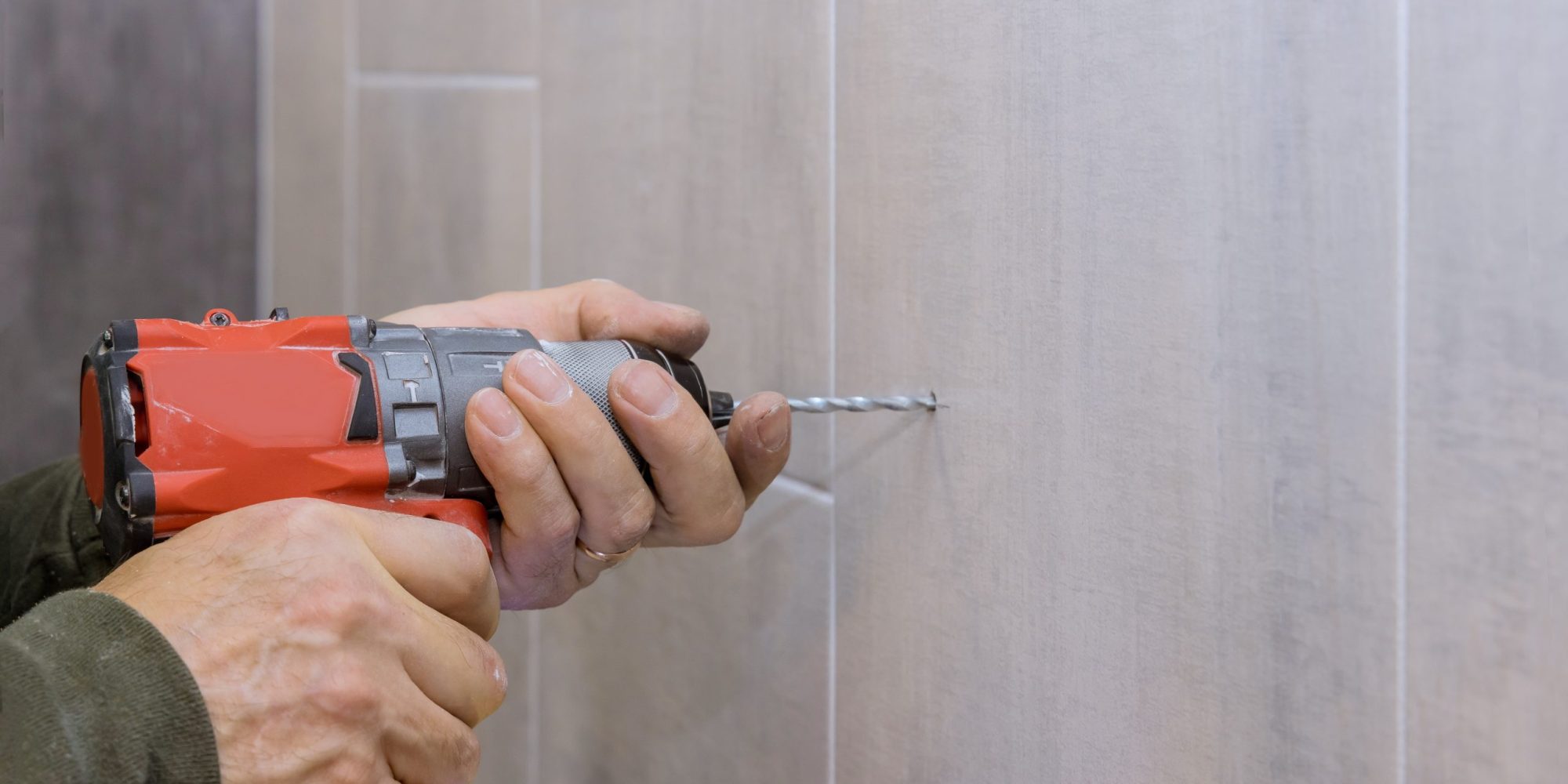 Hands of plumber using a drill to create new holes in tile bathroom wall for installing bathroom accessories